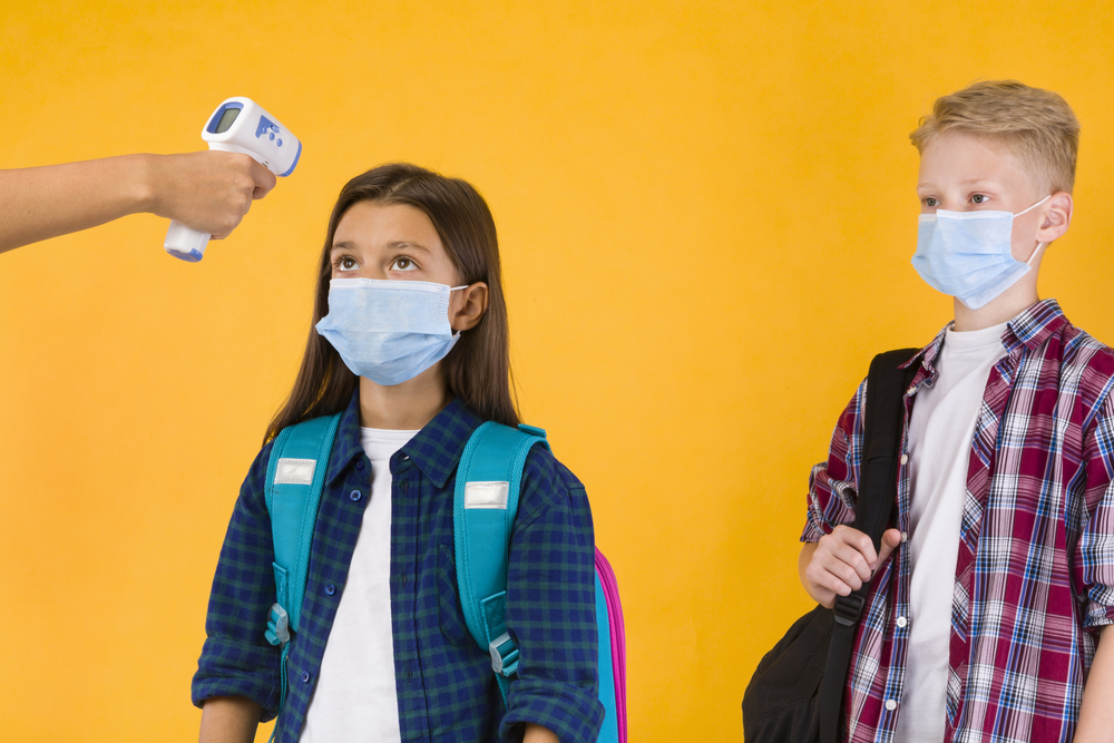 Teacher measuring temperature of children with thermometer